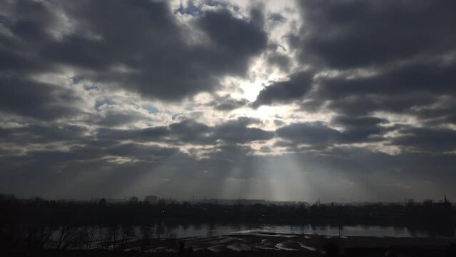 the rays of the sun break through the flying clouds and illuminate the river and coastal buildings on a winter day - timelapse 1 to 30