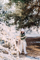 Happy young woman walks in winter forest among pine trees in sunny day.