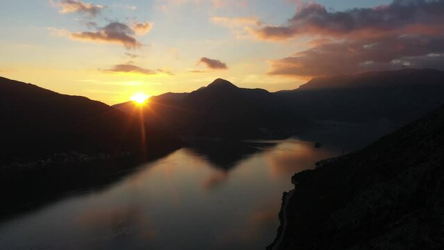 Aerial 4K Drone footage of perast and kotor bay at sunset time, sun is setting behind mountains and colorful clouds reflected on water