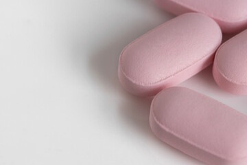 Obraz na płótnie Canvas close up, macro shot of pink, oblong tablet pills on a white background with copy space and shallow depth of field