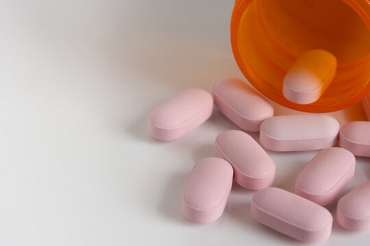 oblong, pink tablet pills spilt from a medicine bottle on a white background with copy space and shallow depth of field