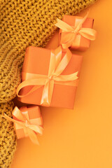 A gift for the holiday..Three small gifts wrapped in orange and with ribbons. A knitted scarf is nearby. Orange background. View from above.