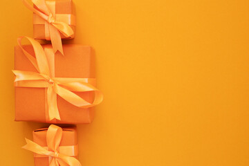 line of three gift boxes with bows on orange background. Space for text. Flat lay