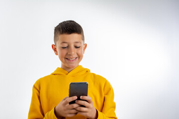 A cheerful child in a yellow hoodie plays games on the phone at home. Happy boy looks at his smartphone.