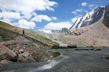 Silhouette of woman standing on rock by lake at foot of glacier. Scenery of Tian Shan Mountains during trekking in Altyn Arashan Valley to glacier. Karakol National Park. Kyrgyzstan, Central Asia