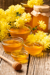 Honey in bowls and yellow flowers on an aged wooden background.