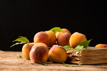 Peaches with green leaves lie on a book and a wooden background.
