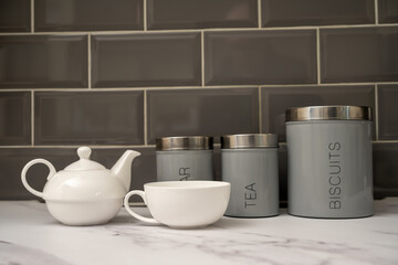 white porcelin china tea pot and cup set on a marble worktop with tea sugar and biscuit cannisters