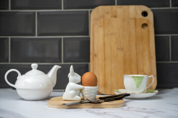 selected focus on the pottery rabbit and basket egg cup with boiled egg against a background of tea pot, bone china cup and saucer on a marble worktop