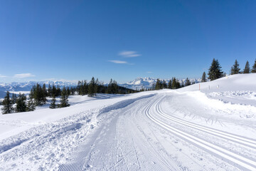 Fototapeta na wymiar Winter mountain landscape, sunny day in Salzburg Alps. Winter road with groomed ski trails.