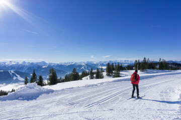 Winter mountain landscape, sunny day in Salzburg Alps. Single cross-country skier on groomed ski...