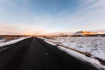 imagen carretera negra entre la nieve con el cielo azul y y unas montañas en el horizonte
