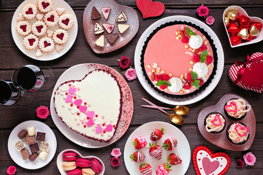 Valentines Day table scene with a selection of desserts and sweets. Top down view on a dark wood background. Love and hearts theme.