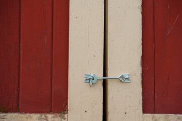 close up of silver door latch on barn door red and white or cream colored barn door with silver or grey hook latch with silver screws to keep barn door closed vertical lines horizontal format backdrop