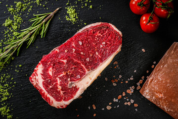 Fresh meat on black board top view. Raw beef steak and red pepper for cooking.
