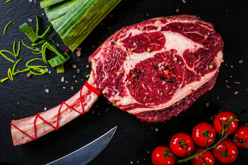 Steak with seasonings on stone background, prime rib eye on bone, top view