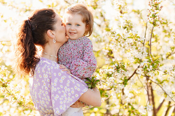 a mother and little daughter in a lilac dresses on a walk in the spring garden. 