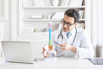 Young handsome male doctor orthopedist demonstrating the problem on spine bone model on the desk in his workplace - obrazy, fototapety, plakaty