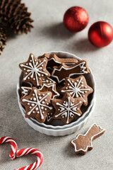White bowl with gingerbread cookies in shape of stars decorated with icing. grey background, red christmas balls, red and white candy canes, pine cones. Homemade traditional winter pastry