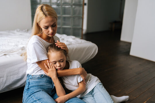 Portrait of tired cute little girl with closed eyes and loving caring mother comforting offended sad child daughter, showing love and care, expressing support, hugging, stroking hair sitting on floor.