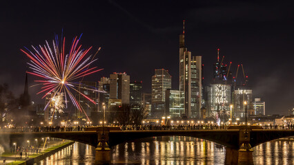 Naklejka premium New years eve with fireworks above the skyline of Frankfurt - Main at night at a cold day in winter with colorful reflections in the water.