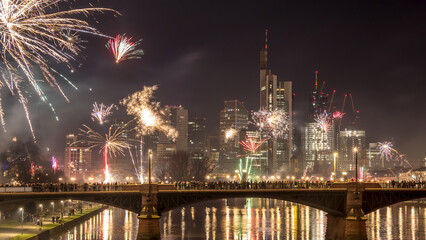 New years eve with fireworks above the skyline of Frankfurt - Main at night at a cold day in winter with colorful reflections in the water.