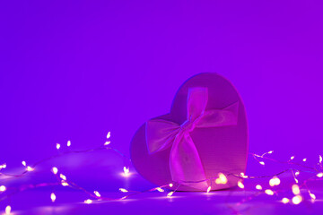 Gift box in the shape of a heart in neon lighting and a garland, the concept of Valentine's day, romance and love, copy space.