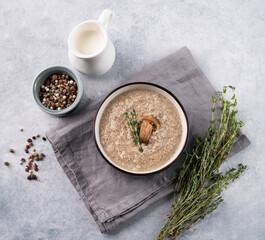 Cream soup of champignons with thyme in a ceramic bowl on a light background with spice and fresh herb. The concept of  healthy and diet food.