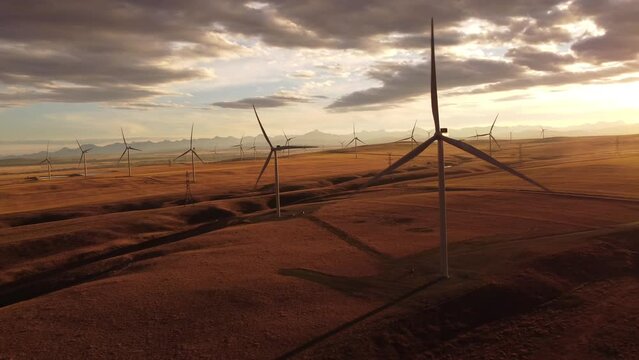Aerial Windmills spinning cinematic shot at sunset over rolling hills and distant mountains.
