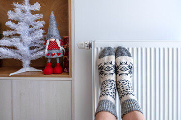 A woman warms her legs in knitted warm socks on a heating radiator