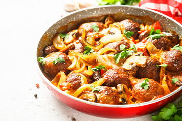 Meatballs with champignon and vegetables stewed in tomato sauce in a frying pan. Top view with copy space at light stone table.