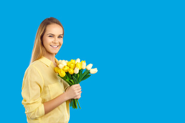 Obraz na płótnie Canvas Smiling young Caucasian woman with flowers celebrate international women day. Happy female isolated on blue studio background hold floral bouquet for mothers holiday. Copy space.