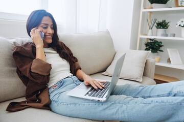 Woman blogger with phone lying at home and talking on the phone on sofa with laptop and working freelancer online, selfie