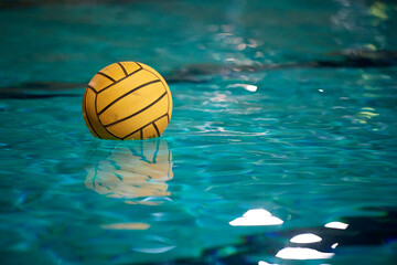 Yellow water polo ball in a swimming pool on blue water background. Film noise and gain - 558486160