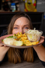 Cheerful woman gesturing hold in hands plate with fries, chicken fillet and vegetable salad. Serving of main dish and garnish closeup, selective focus on human. Love food, restaurant dish, meal