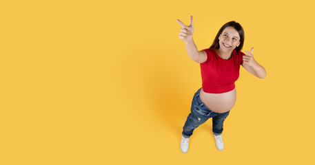 Fototapeta na wymiar Above Shot Of Pregnant Woman Pointing At Copy Space On Yellow Background