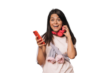 Waist up shot of excited girl in casual clothes listening music with headphones holding phone being in good mood isolated on transparent background. People sincere emotions, lifestyle concept.