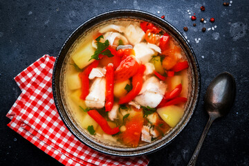 Fish soup with cod, paprika, potatoes, tomatoes and parsley in ceramic soup bowl on dark table...