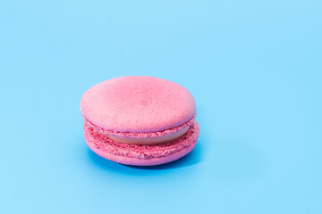 Pink french macaroon or macaron on blue background. Tasty colourful macarons. Cookie made of two smooth halves, fastened with stringy fillings. French pastry made from egg whites.