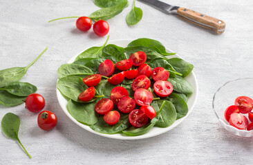 Plate with fresh spinach leaves and cherry tomatoes on a light gray background. delicious healthy food
