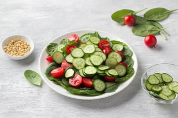 Plate with fresh spinach leaves, cucumbers, cherry tomatoes and pine nuts on a light gray background. delicious healthy food