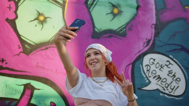 Redhead woman taking selfies on smartphone against urban street art