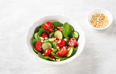 Plate with salad of fresh spinach leaves, cucumbers, cherry tomatoes and pine nuts with dressing on a light gray background. delicious healthy food
