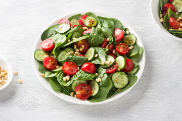 Plate with salad of fresh spinach leaves, cucumbers, cherry tomatoes and pine nuts with dressing on...