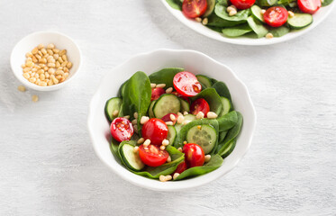 Plate with salad of fresh spinach leaves, cucumbers, cherry tomatoes and pine nuts with dressing on a light gray background. delicious healthy food
