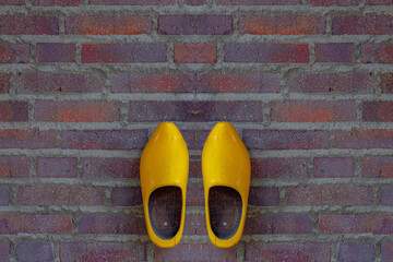 Selective focus of traditional yellow wooden shoes or clog on brick wall as background, Old pair of vintage and classic wooden shoes, Typical rural farmhouse in countryside villages in Netherlands.