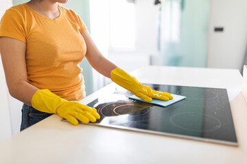 Housekeeping Concept. Young Woman In Rubber Gloves Cleaning Induction Cooktop With Rag