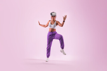 Young black woman dancing in metaverse, having fun while wearing virtual reality goggles, pink background, neon light