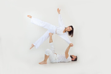 Fit couple on white background. Middle-aged man lying holding with hand young woman stretching leg, practicing acroyoga.