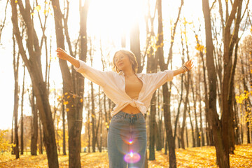 Portrait of young happy teenage girl standing on yellow fallen maple leaves, stretching hands...